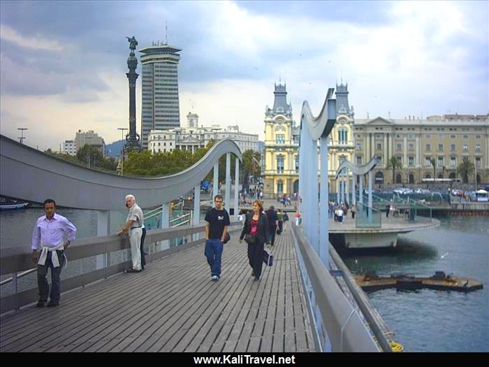 People walking across wood deck bridge in Barcelona harbour.