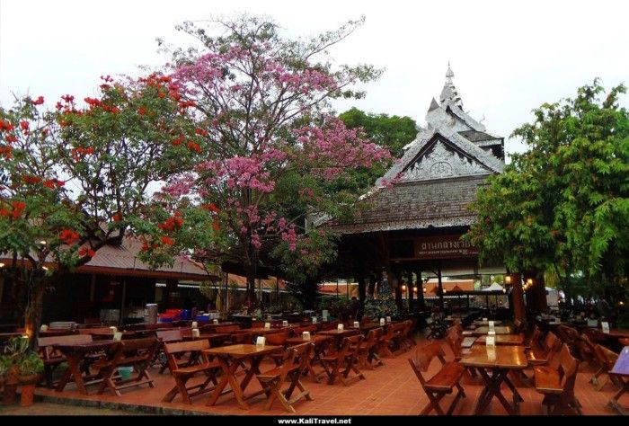 Chiang Rai restaurant terrace with pagoda, flowering trees and wood benches.