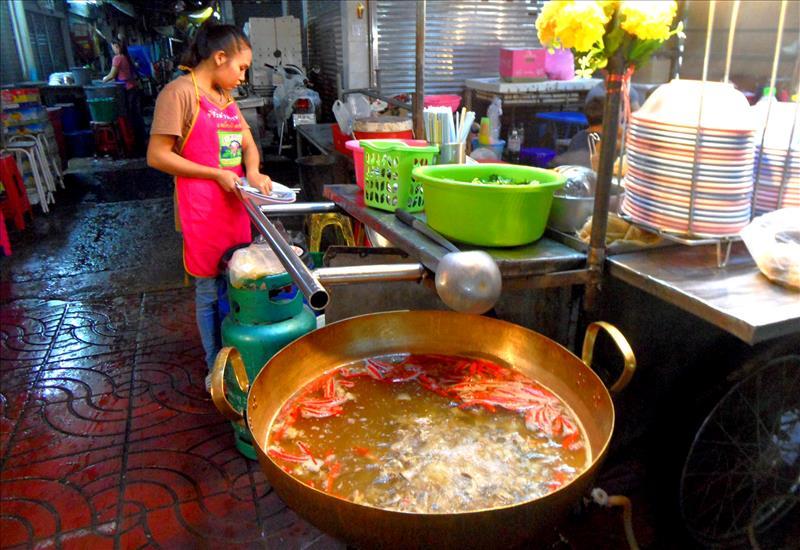 Young woman cooking seafood soup in huge metal pot in Bangkok.