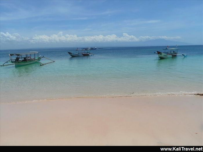 Boats in the sea by the sandy pink beach.