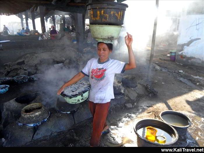 Lady with bucket on her head surrounded by steam from the fish salting.