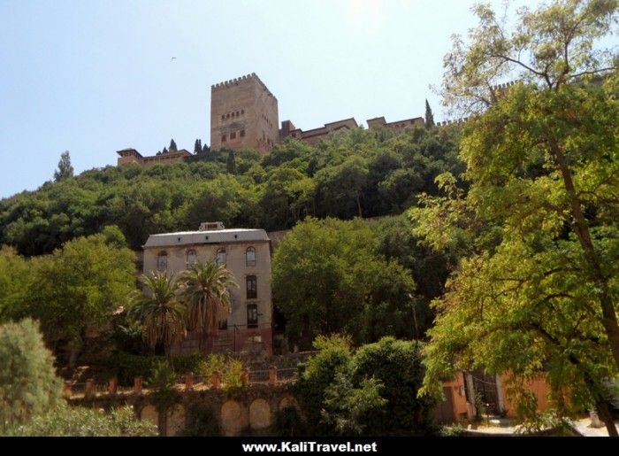 Paseo De Los Tristes con La Alhambra al fondo entre árboles.