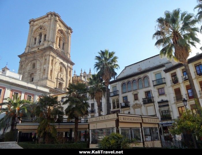 Restaurant terrace in Plaza Romanilla surround by historic buildings and Granada Cathedral bell tower.