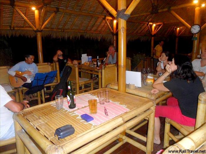 Lombok man playing the guitar to people sitting in the bamboo eco lodge.