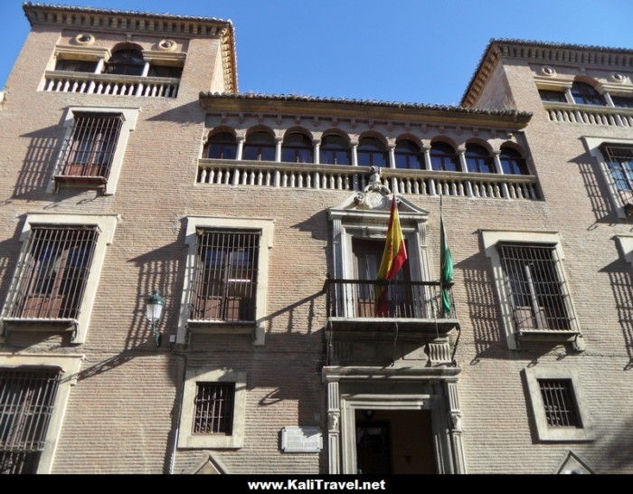 Edifico antiguo de ladrillo con rejas en las ventanas y la bandera de España.