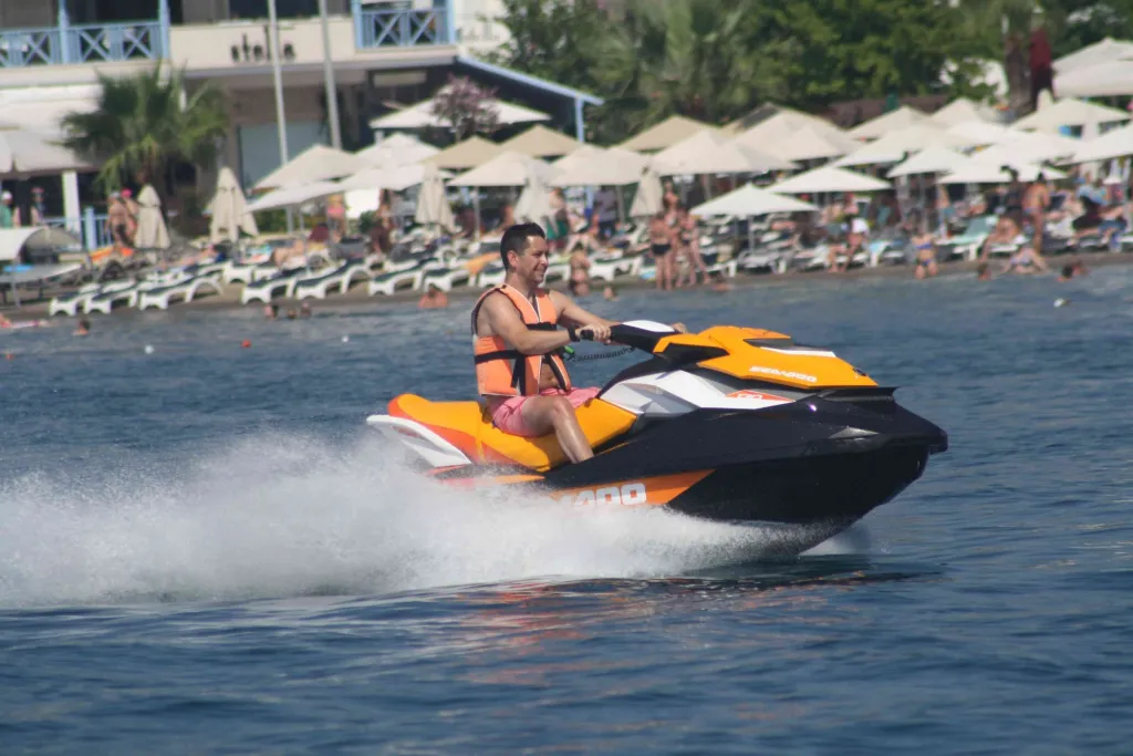 Jet skiing in the turquoise sea just off a beach with sun umbrellas and loungers.