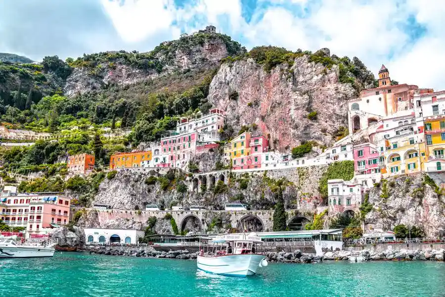 Amalfi coast with colourful houses on the cliff face, and leisure boat in the sea.