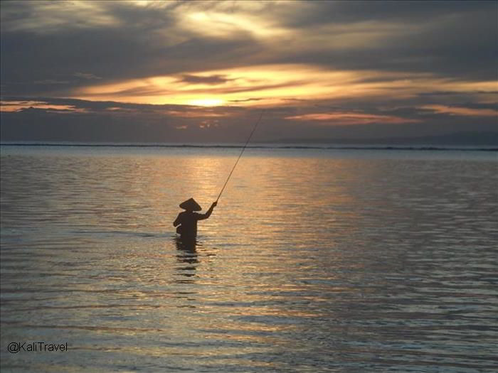 Fisherman at sunrise in the sea at Sanur beach in Bali.