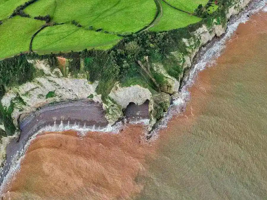 Aerial view of the sea, headland cliffs and grassy downs.