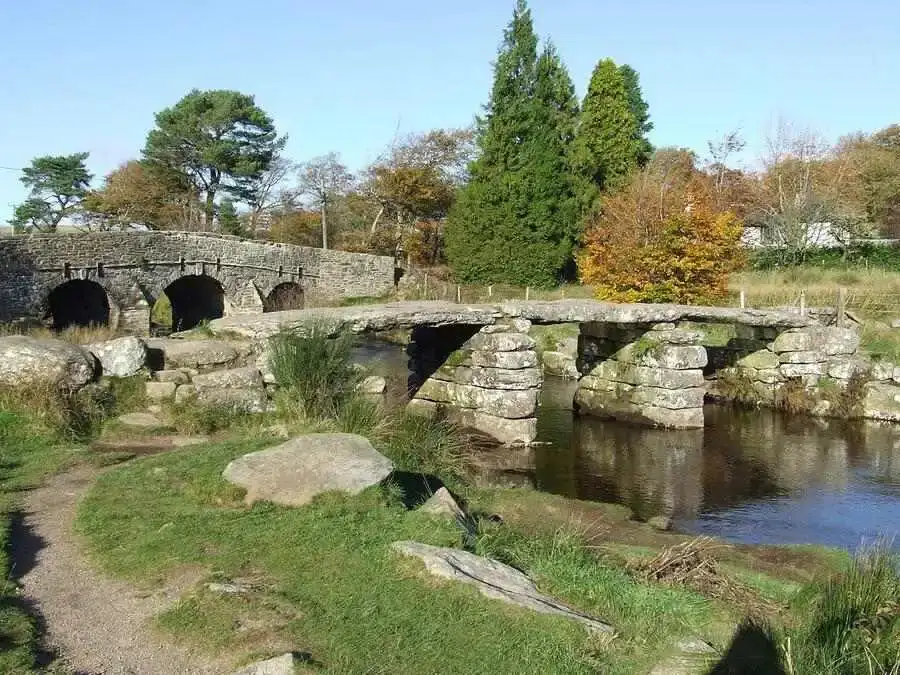 Narrow river with an ancient clapper bridge and a second 3 arch stone bridge behind.
