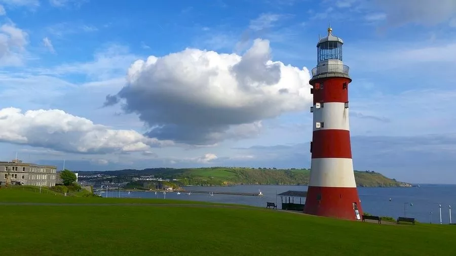 Landmark red and white lighthouse tower on grassy plain by the sea.