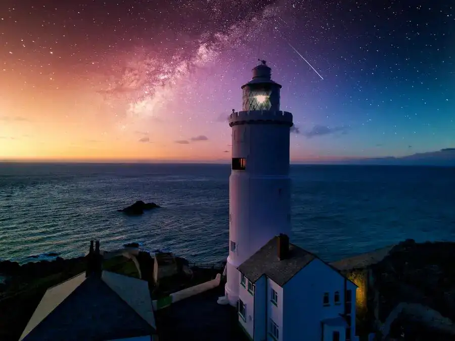 Lighthouse overlooking the sea and a twilight sky with sunset and stars.