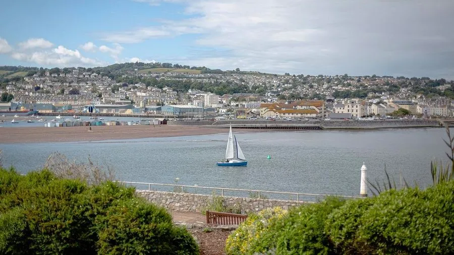 Yacht in the bay with leisure harbour and town on the hillside in distance.