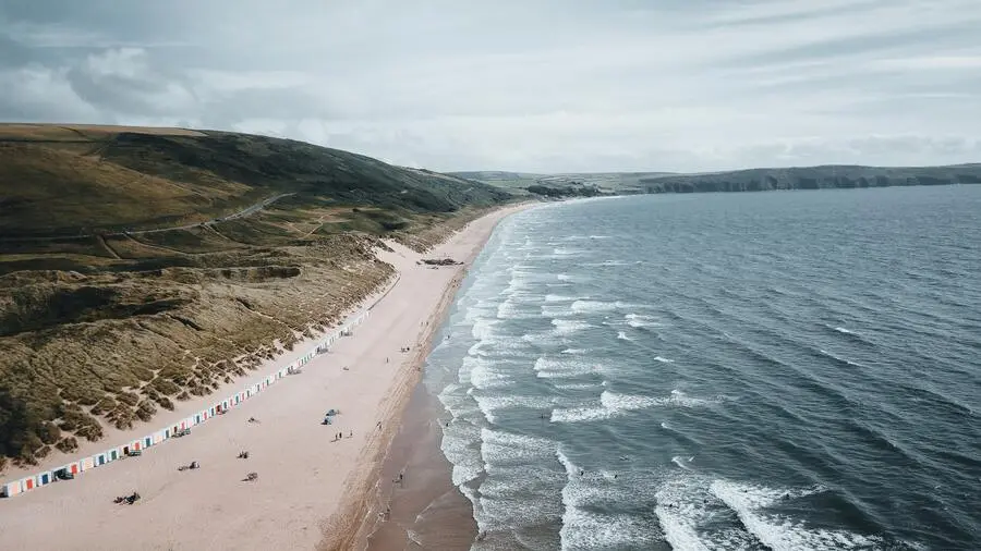 Very long white sand beach beside grey sea with surf.