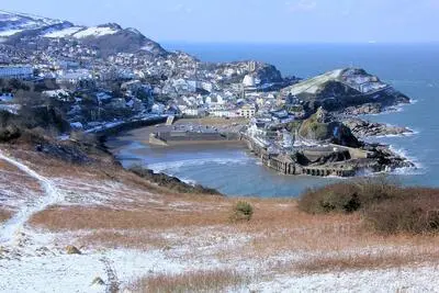 Headland with sprinkling of snow, and a viilage, harbour and the sea below.