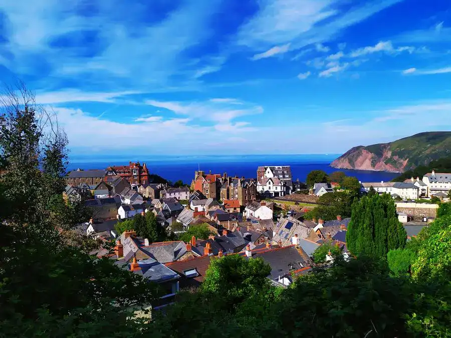 View over slate rooftops to blue sea with cliffs in the distance.