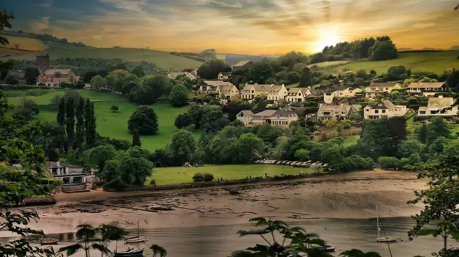 Sunset views over a river with village cottages and a church on the grassy hillside.