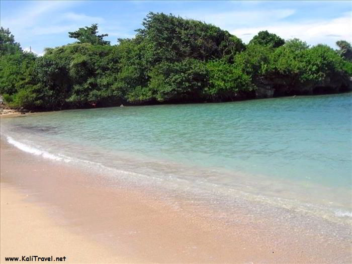 Golden sands, calm blue sea and green trees by Nua Dusa beach on Bali.