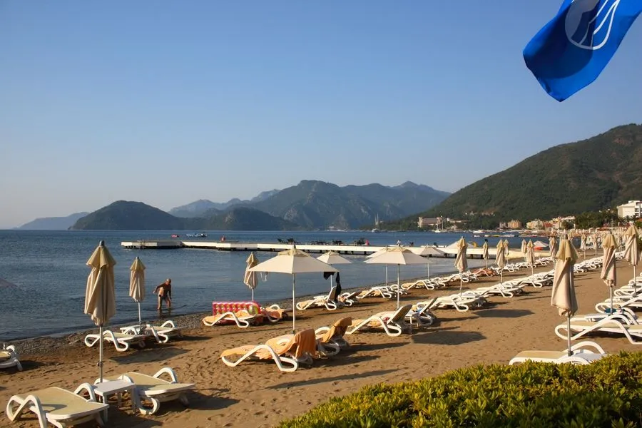 The long sandy beach with sun loungers, turquoise sea, and hills on the coast