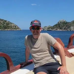 Man sat on a boat sailing off the turquoise coast.