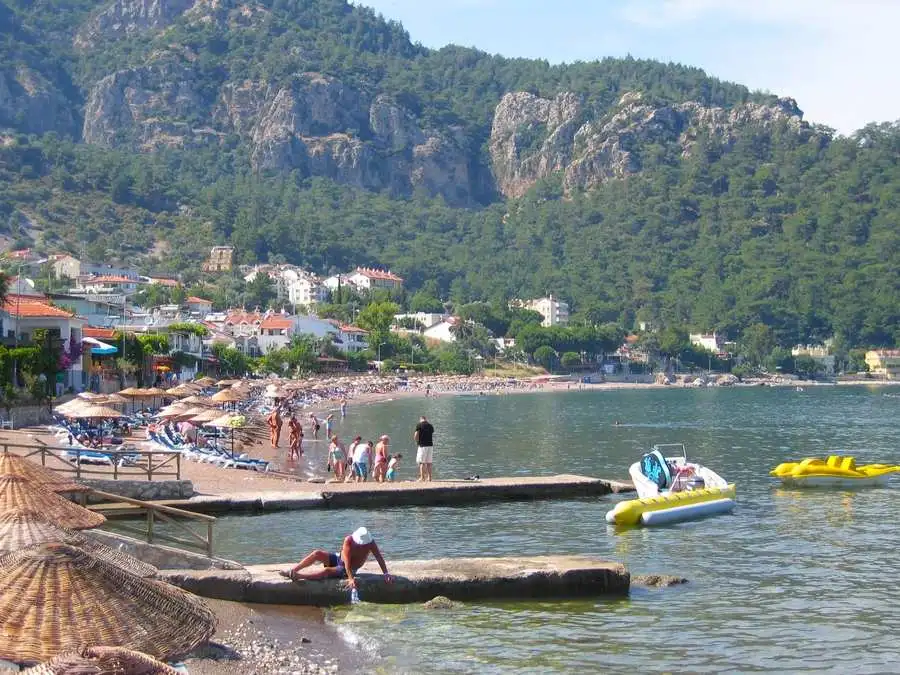 People on the sandy beach, mountains behind, and banana boats in the sea.