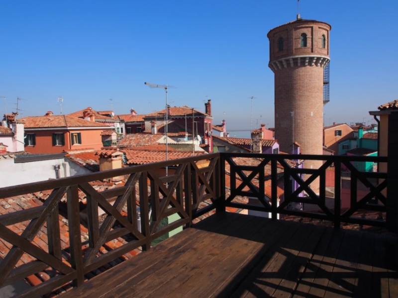 Burano Sky House terrace view over rooftops and a tower, Venice Lagoon Islands.