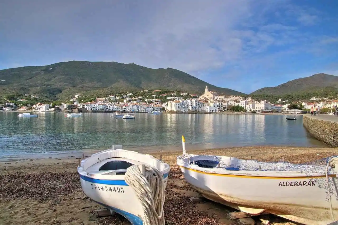 2 rowing boats on the beach by the sea with Cadaques village across the waters.