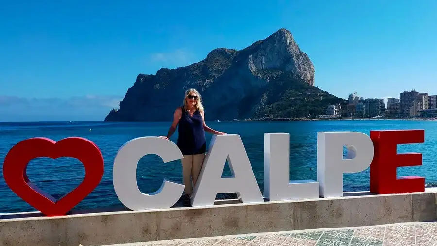 Large 'Calpe' sign on seafront with huge Calpe rock across the sea in background.