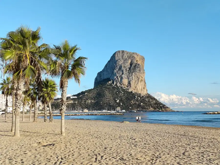 Sandy beach with palms in front of Peñon de Ifach in Calpe, Spain