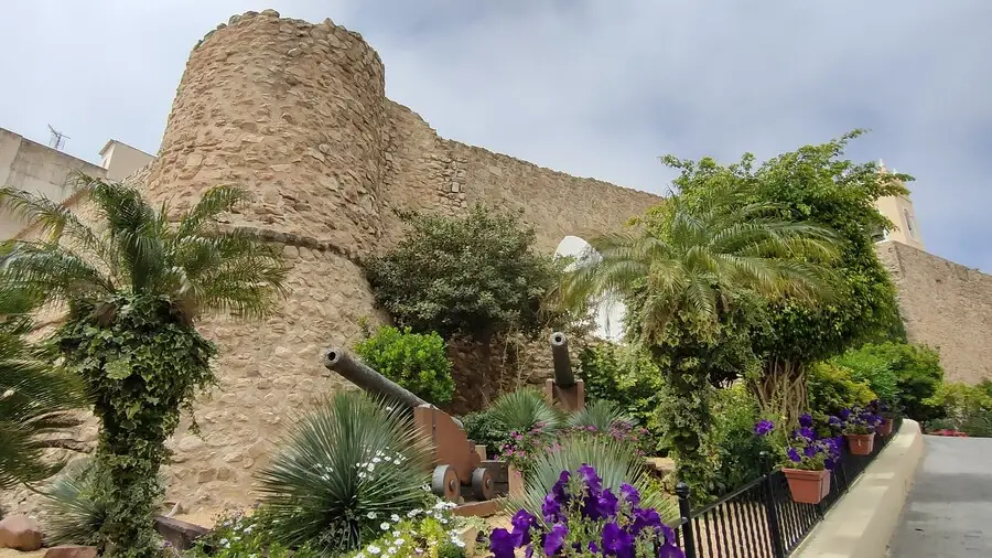 Calpe's old town walls with cannons, flowers and a stone turret.