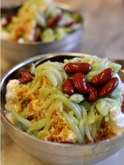 Bowl of cendol green noodles dessert with red kidney beans.