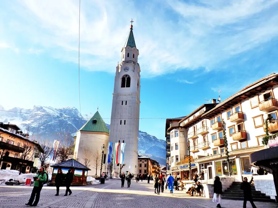 Cathedral tower in cobblestone square with snowy mountains in background.