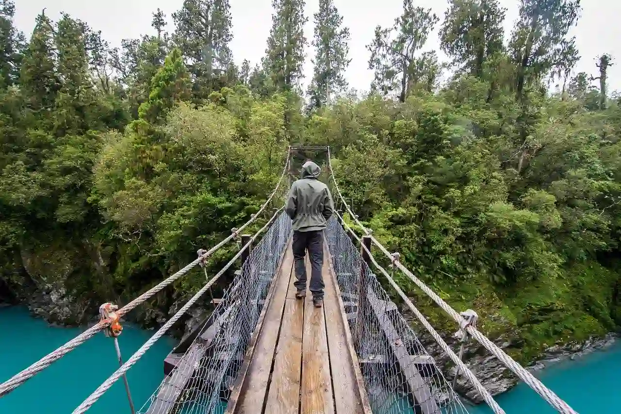Person hiking across a wooden bridge suspended over a river gorge.