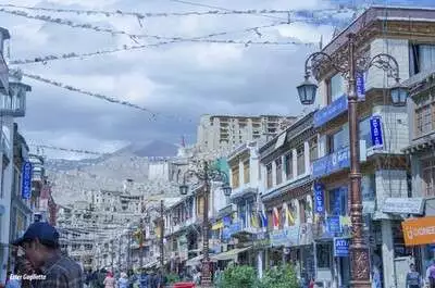 Calle con antiguas edificios con comercios con montañas al fondo.