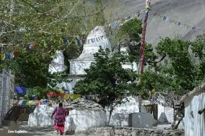 Una mujer y banderas de oración delante de una estupa rodeado de árboles.