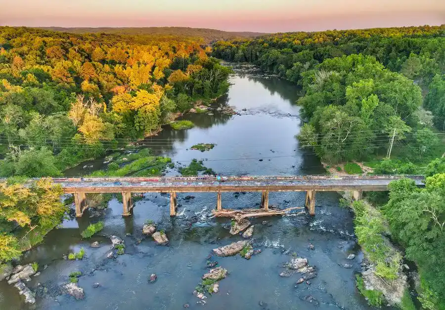 An old bridge crossing a river with fir trees on the banks.