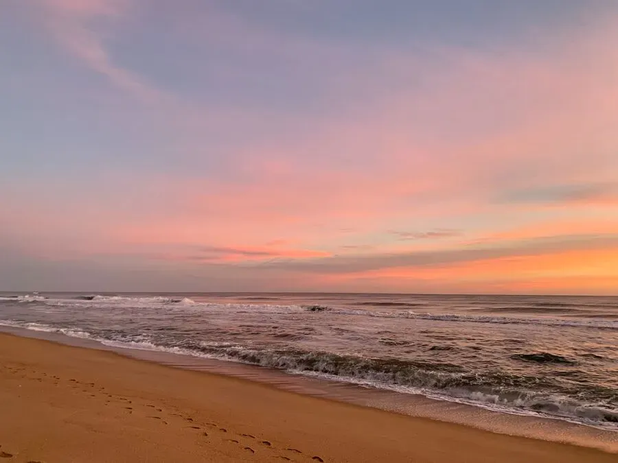 Orange pink skies at daybreak over a sandy beach and the ocean.
