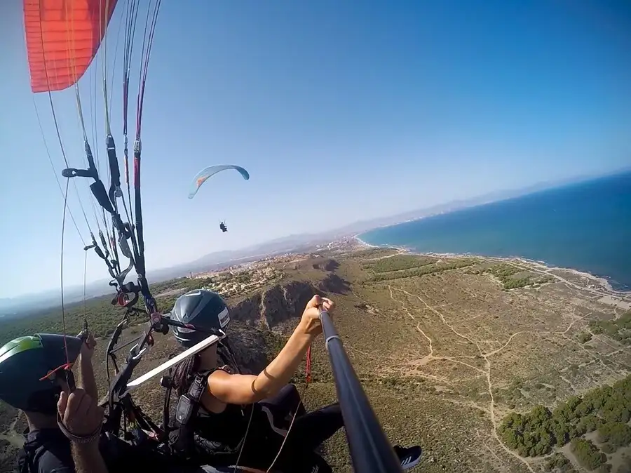 Selfie stick shot of a couple tandem paragliding in Alicante over the coast.
