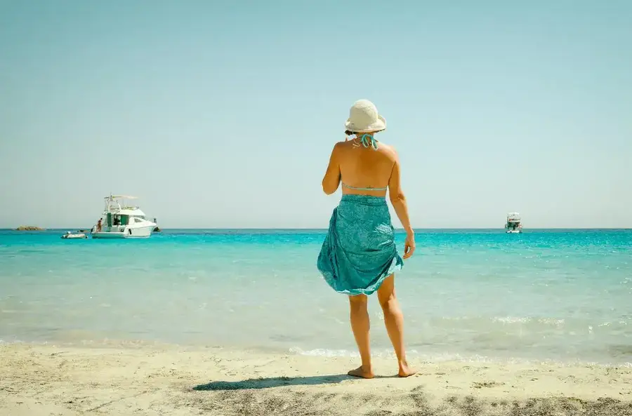 Woman standing on sandy beach with yachts out to sea.