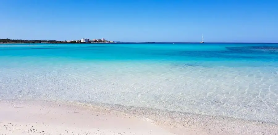 White sandy beach and turquoise sea with sailing yacht in distance. 