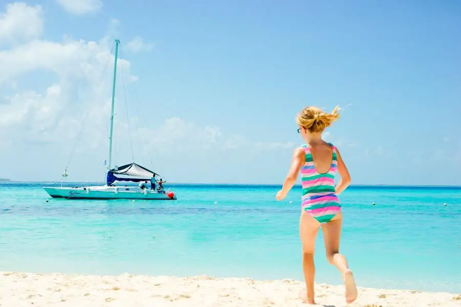 Little girl running on sany beach with sailing boat in the sea.