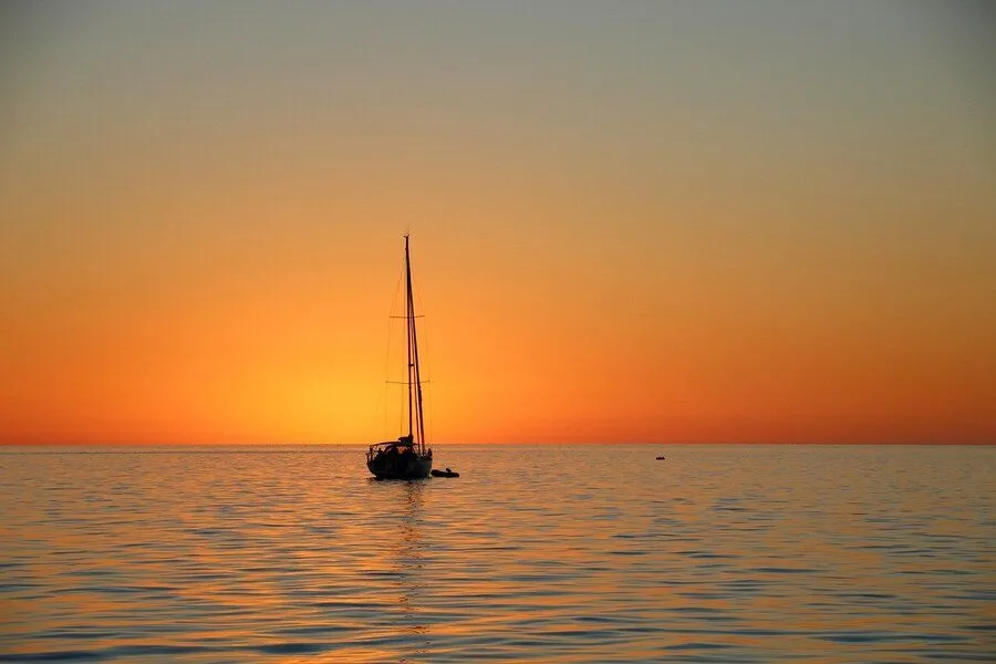 Tall masted sailing boat in the ocean at sunset.