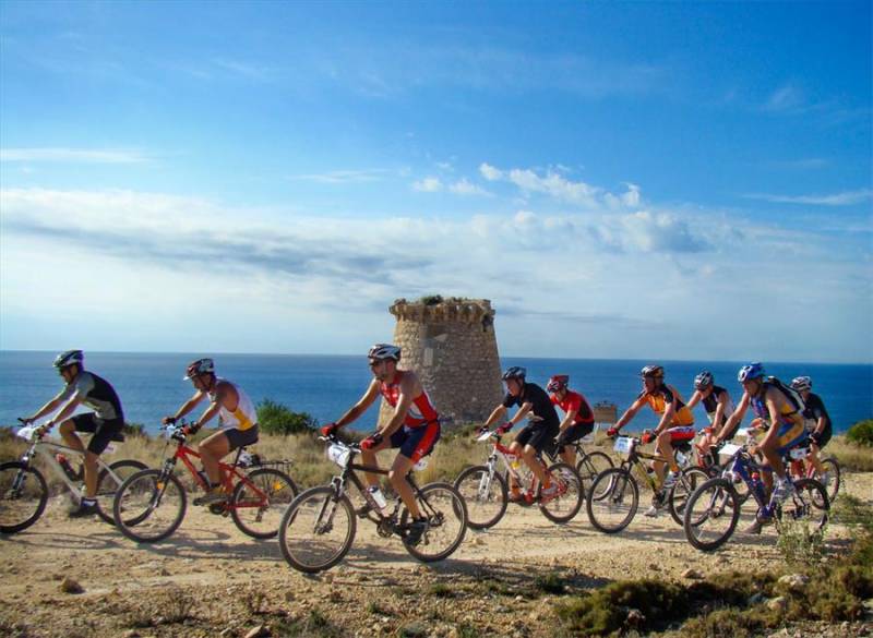Cyclists race past old watchtower and Mediterranean sea in Costa Blanca.