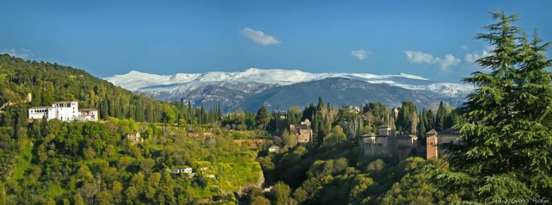 Historic building among pine trees with snow-capped Sierra Nevada the mountains of Granada in the background.