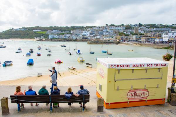 Cornish icecream booth, visitors looking at boats in St Ives harbour.