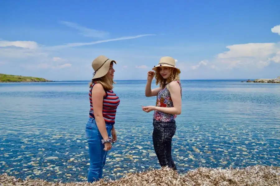 2 women travellers wearing summer hats, standing by a lake in the Balkans.