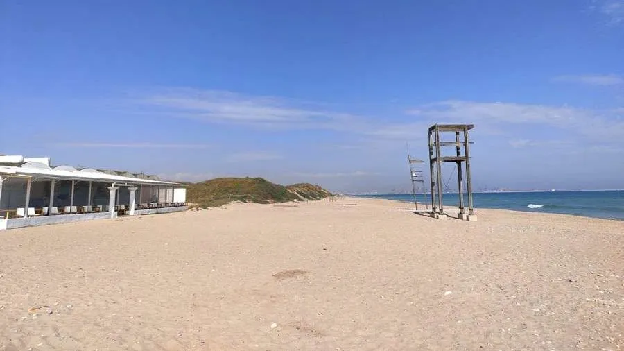 Playa de arena dorada con resturante y dunas a la izquierda y el mar a la derecha.
