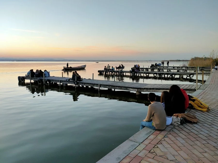 Gente sentando en el muelle de Mirador de Pujol contemplado el Lago de la Albufera al atardecer.