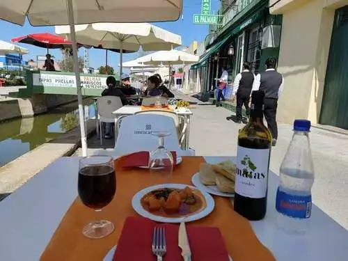 Ración de all i pebre y copa de vino tinto sobre una mesa de restaurante a lado del canal.