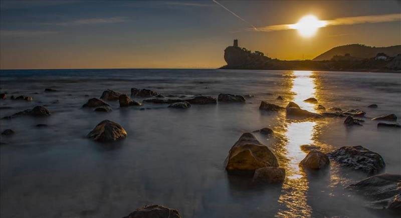 Sunset over the Mediterranean sea and watchtower at Charco Beach in Villayoyosa, Costa Blanca. 